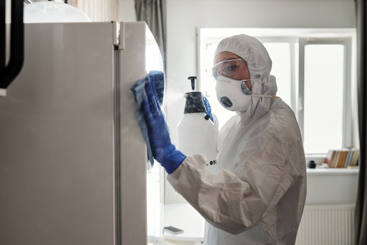 Person in protective gear sanitizing refrigerator at home for safety.